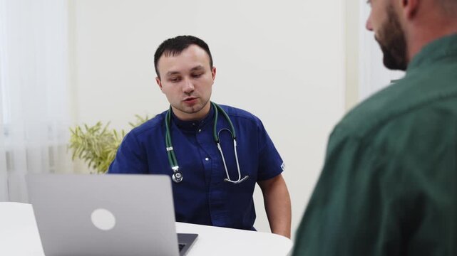 Family physician explaining medical information to a young man using a laptop during a consultation. Concept digital healthcare, primary care, patient education, medical technology, clinical practice.