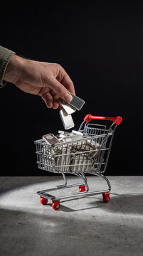 Man hand putting silver bar into miniature shopping cart. Investment concept for precious metal purchase. Financial asset accumulation and buying bullion for wealth savings protection.