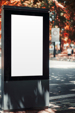 Vertical advertising template on an empty illuminated street display, with soft-focus pedestrians, vivid autumn foliage and dappled sunlight along an urban sidewalk