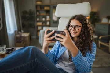 Smiling girl playing mobile game on smartphone at home © Miljan Živković