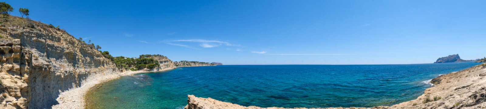 panoramic view of the rocky Mediterranean coastline at Cala de la Llobella in Benissa with turquoise water and cliffs under a clear blue sky on a sunny summer day