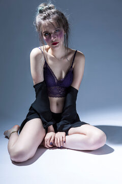 Violence and Harassment Ideas. Young Caucasian Girl in Violet Nightie and Black Shirt Sitting and Posing on Gray Background With Bruses Under Eyes on Face.