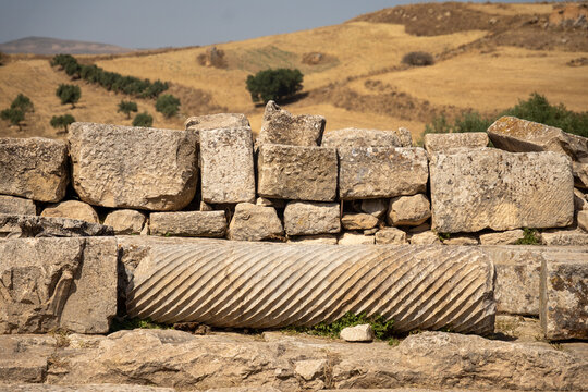 Broken column in front of piled stones at the archaeological site of Dougga, in Teboursouk, outside of Tunis, Tunisia