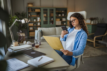 Teen girl studying homework holding smartphone and documents at home
