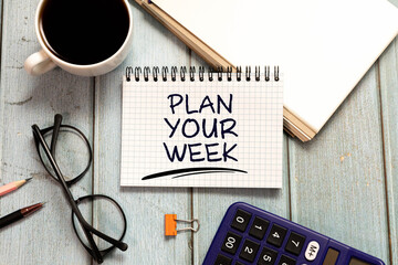 Naklejka premium Plan Your Week Message on Spiral Notebook with Coffee and Office Supplies.