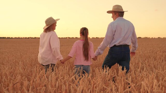 Parents dad mom child daughter walking hand in hand through wheat field. Farming family, group people united by common idea. Happy farming family with child go through wheat field. Family hugging Love