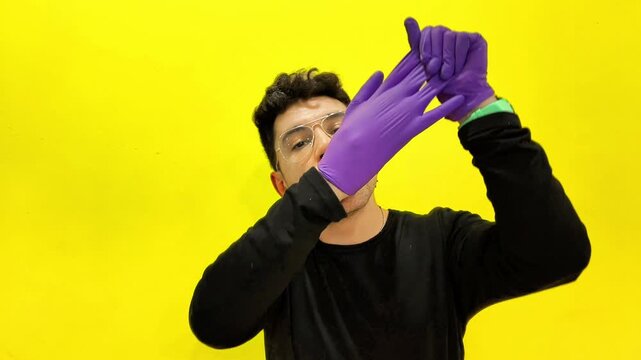 Young man performing magic trick inflating a purple glove against a yellow background