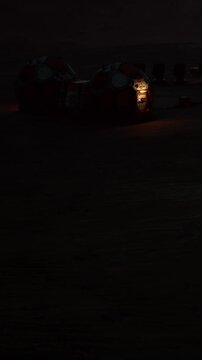 A lander is positioned in a dark desert area at night. The faint glow of the light from the lander reveals part of the rough terrain around it. The scene appears solitary and quiet.