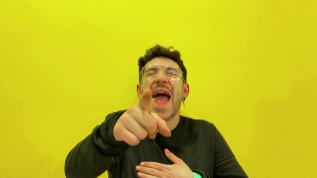 Young man mocking and laughing at the camera on a yellow background