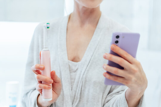 Close up woman puts settings of his electronic toothbrush with mobile phone app. Wireless connecting sonic toothbrush with smart phone app. Modern home health care technology concept. Selective focus