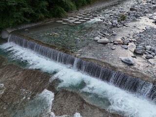 Clear water cascades over a small, natural waterfall. Rocks line the streambed beneath the falling water. Greenery borders the water's edge above the cascade. The scene evokes calm © Masakazu Tokashiki