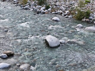 Clear stream flows over smooth stones. Rocks dot the water's gentle path. Green plants peek from riverbanks. Peaceful current whispers through gravel. Ideal for nature, travel, or environmental themes © Masakazu Tokashiki