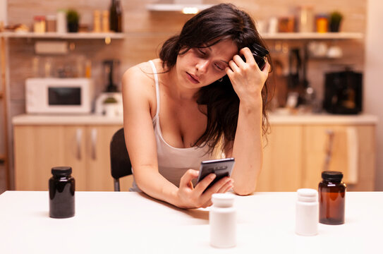 Stressed tired woman sits with pills while suffering migraine, anxiety and depression symptoms, showing a private health worry at home.