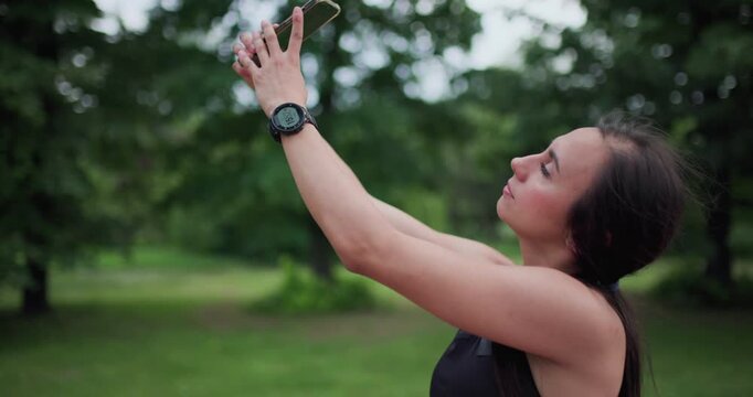 A fit young woman in athletic wear takes a selfie with her smartphone in an outdoor park, embracing a healthy and active lifestyle.