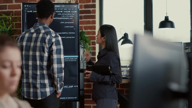 System engineer studies wall screen code during a debugging session with a digital tablet, linking error checking, while reviewing developer feedback.