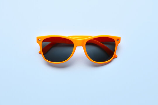 Stylish sunglasses with orange frame on light blue background