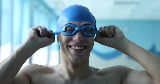 Smiling man in swim cap putting on goggles at indoor swimming pool