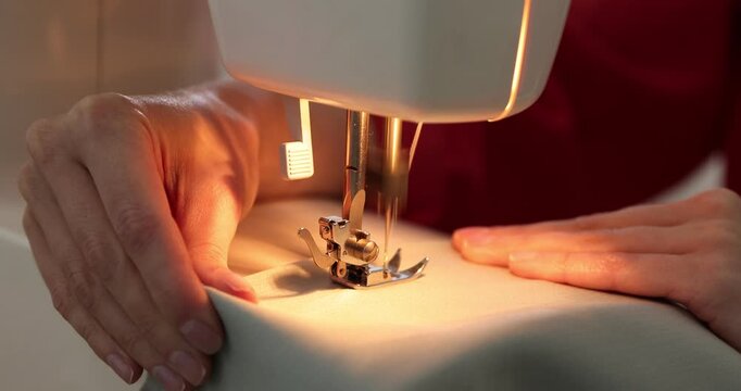 Woman sewing fabric with professional machine at table in workshop, closeup