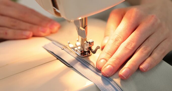 Woman sewing fabric with professional machine at table in workshop, closeup