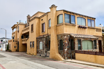Fototapeta premium Mediterranean style luxury villa exterior with warm stucco facade, natural stone accents, terracotta roof tiles and elegant balconies on a coastal California street.