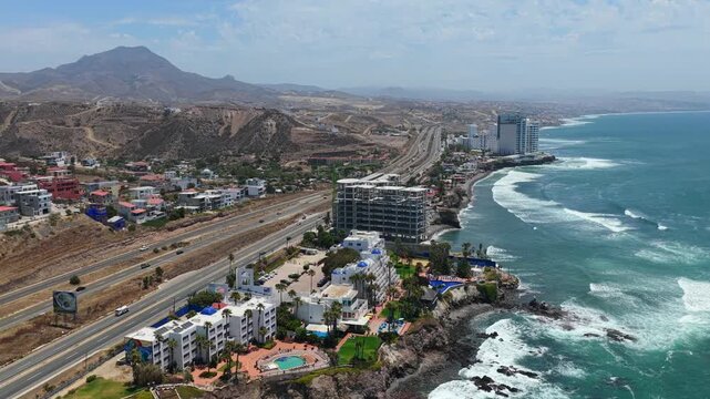 Aerial orbit over Las Rocas Resort and Spa on the Rosarito coastline reveals the Christ of the Sacred Heart hilltop monument in Mexico