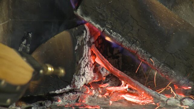 Close-up of fireplace bellows stoking flames, sparks and glowing embers around burning firewood in a cozy home hearth.