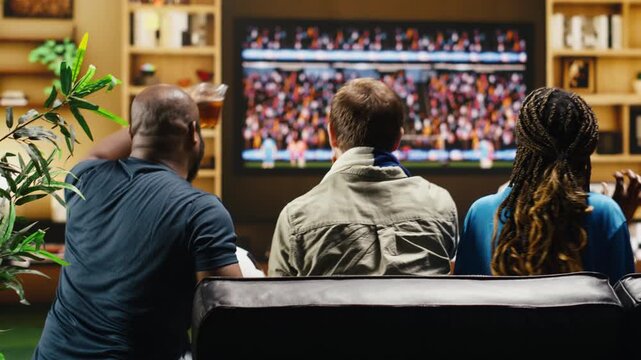 Soccer supporters at home react angrily to referee call, gesturing toward TV during dramatic match while football fans on apartment couch shout in frustration, loudly protesting during live game.