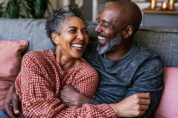 Fototapeta premium Happy mature African American couple laughing together on sofa at home