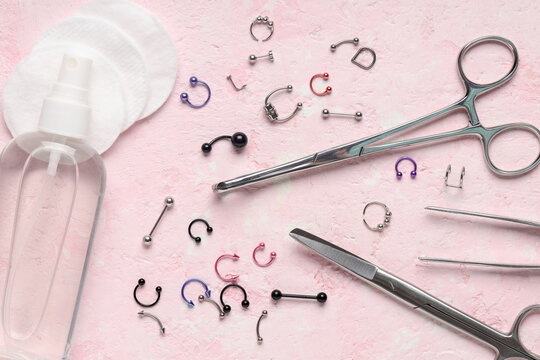 Body piercing jewelry and tools with antiseptic spray and cotton pads on a pink background