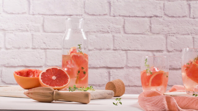 Refreshing grapefruit infused water in a glass bottle and glasses on a rustic wooden table