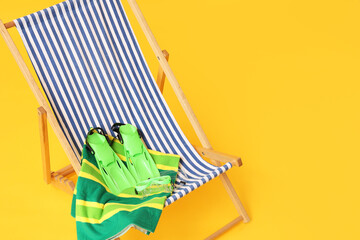 Striped beach chair with green flippers and swimming goggles on a yellow background, summer vacation © Pixel-Shot