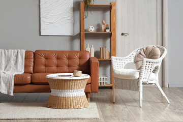 Cozy living room interior with brown leather sofa, white wicker chair, and wooden bookshelf against a gray wall © Pixel-Shot