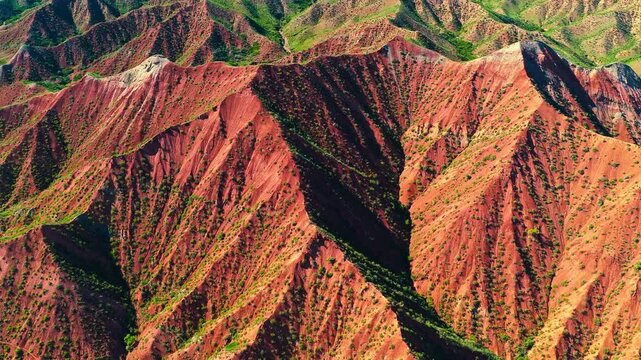 High angle view of dramatic red sandstone mountain ridges and deep canyons with green vegetation in Xinjiang, China.