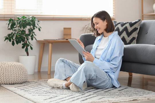 Young woman using modern tablet computer on carpet at home