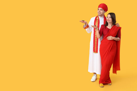 Beautiful Indian couple with diya lamps on yellow background