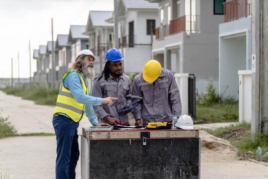 Senior Engineers discussing blueprint at housing construction site during daytime, concept of teamwork and residential project management, Real estate property development industry.