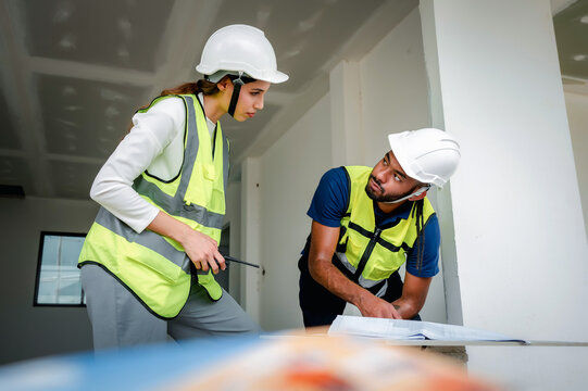 Construction Manager analyzing building blueprint indoor with Civil engineer while holding walkie talkie, scene for real estate property development and professional engineering work at site
