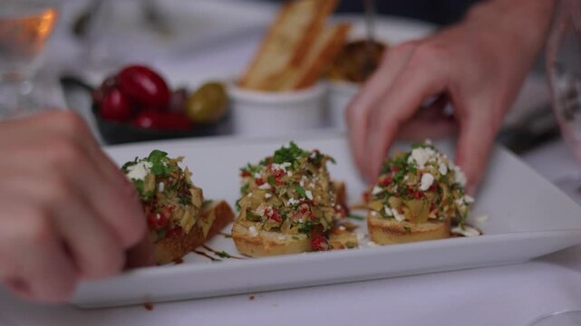 Hands reaching and taking bruschetta appetizers from restaurant plate