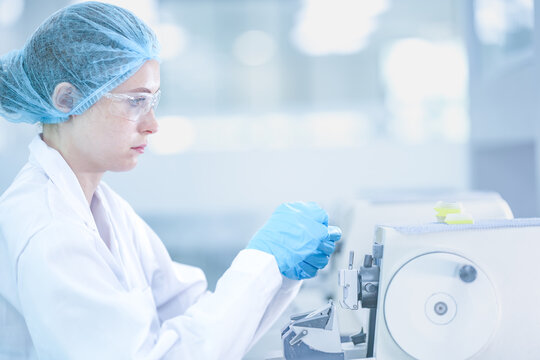 Professional histology technician cutting tissue section with rotary microtome. Female scientist in safety gear processing paraffin biopsy block in lab.