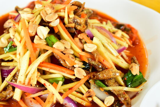 Thai spicy green mango salad serve on white plate, flavors of traditional Thai cuisine