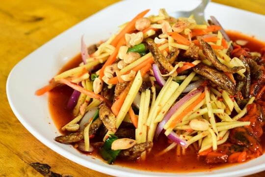 Thai spicy green mango salad serve on white plate, flavors of traditional Thai cuisine