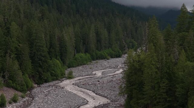 Aerial of muddy brown Nisqually River in Mount Rainier National Park in summer surrounded by forest with dark misty clouds