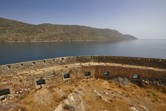 Ancient stone wall overlooking a calm sea with mountains in the background under a clear blue sky, Venetian Sea Fortress, Leprosy Island, Spinalonga, Elounda Bay, Mirabello Bay, East Crete, Crete, Greek Islands, Greece