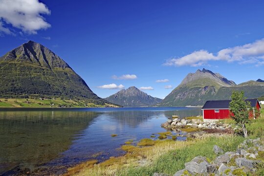 Red wooden house and high, rugged mountains by a fjord, shallow bay, Aldersund, FV 17, Kystriksveien, Nordland, Norway