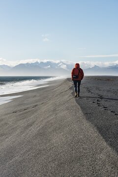 Man walking by the sea in the black sandy beach, lava beach, snow-capped mountains, Hvalnes Nature Reserve, South Iceland, Iceland