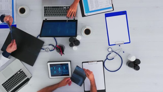 Medical team takes notes and analyzes x ray material around a desk with stethoscope and digital devices, creating a flat lay clinic conference setup with copy space.