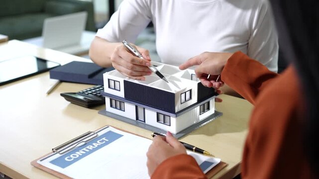 Business people discussing a house sale with a model home and contract on a desk in an office