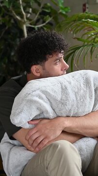 Heartbroken young man hugging pillow on couch feeling lonely at home