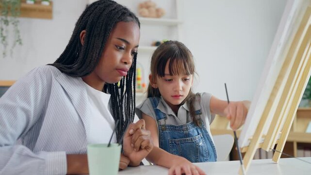 African woman tutor guide young child through art and painting in nursery. 