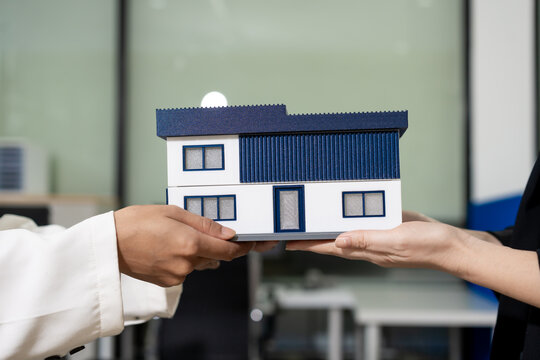 Two people exchanging a small house model, representing home buying, selling, property deal, and real estate service